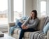 A woman sits on a sofa rubbing her foot with a pained facial expression.