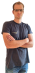 Junger Mann mit Brille und verschränkten Armen trägt ein dunkles T-Shirt mit dem Logo der Energieberatung Bau-Mann.