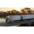 Grauer Volvo LKW mit zwei Anhängern fährt bei Sonnenuntergang über eine Brücke.