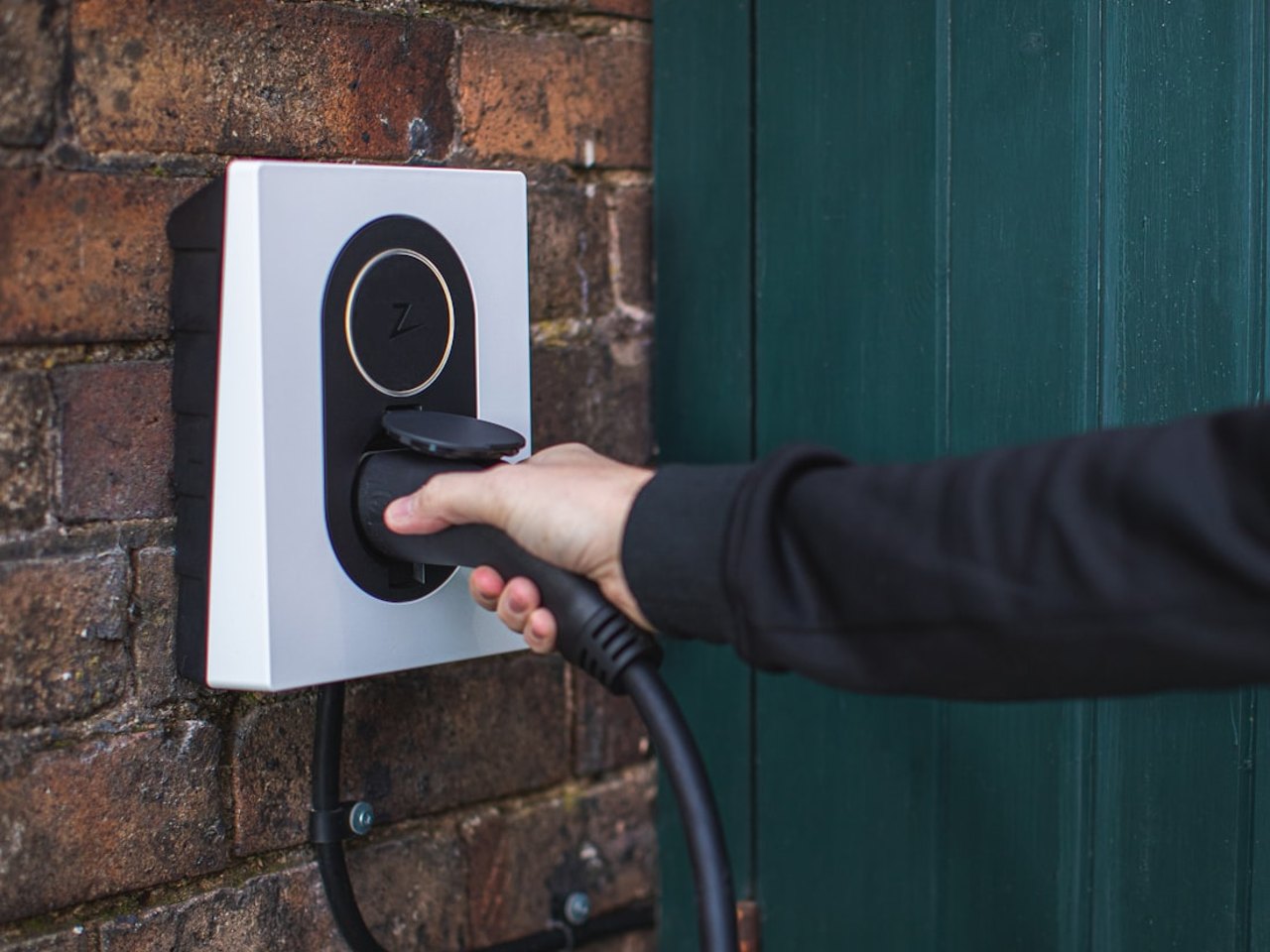 Hand holding a charging connector at a wall-mounted EV charger