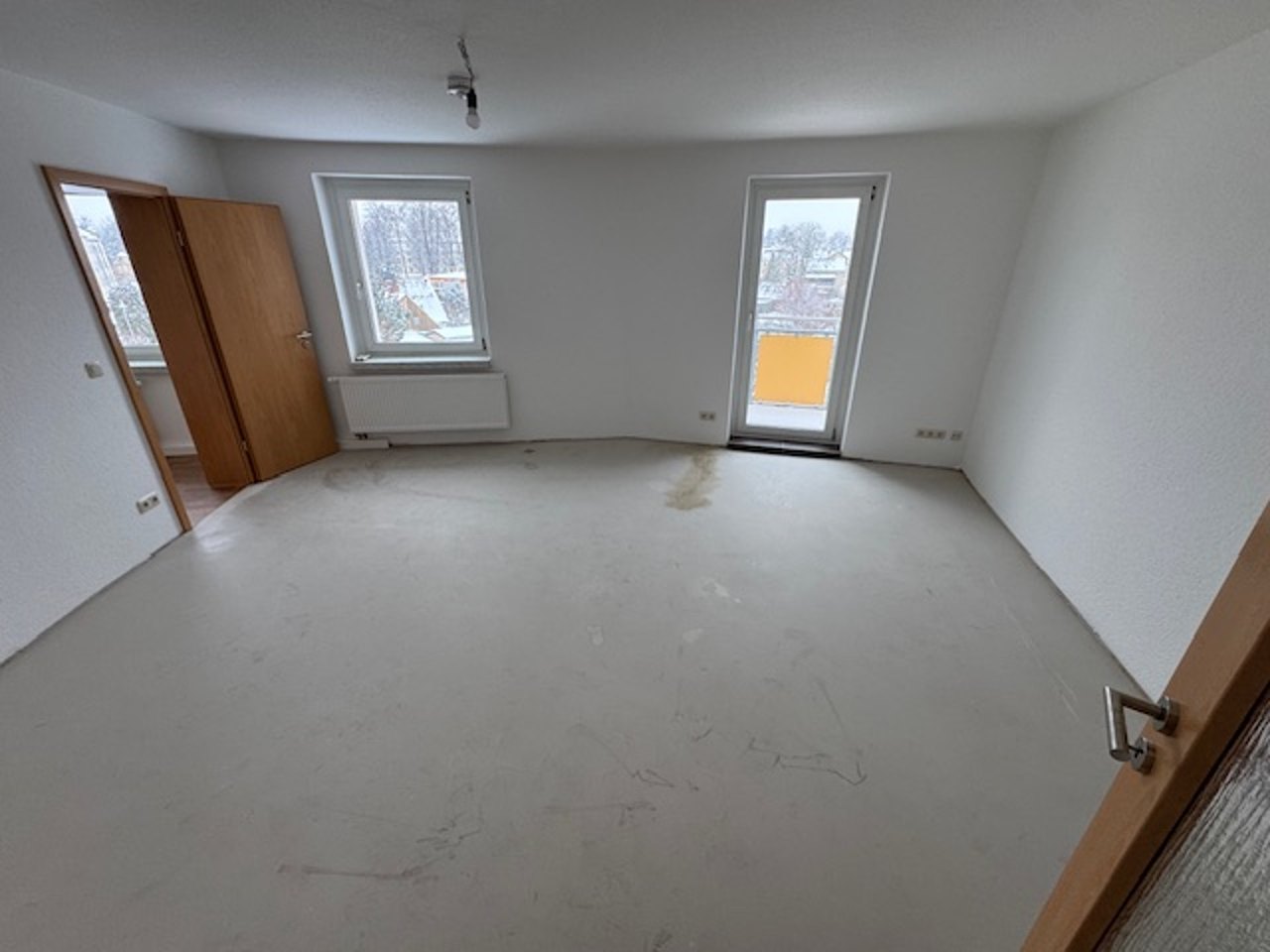 Leeres Zimmer mit drei Fenstern und unverlegtem Boden