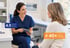 A female nurse in blue scrubs holds a tablet while speaking to a patient, with 4.9 rating and 40+ years experience badges.