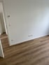 Leere weiße Wände mit braunem Holzboden, Thermostat und Steckdosen.