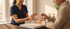 A nurse in blue scrubs hands a weekly pill organizer to an elderly man in a sweater.