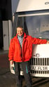Ein lächelnder Mann in einer roten Jacke und dunkler Hose steht vor einem weißen Wohnmobil mit dem Kennzeichen "ERZ FL 19".