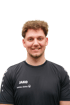 Mann mit kurzen, hellbraunen Locken und Silberkette im schwarzen JAKO-Trikot mit SIGNAL IDUNA-Logo vor weißem Hintergrund.
