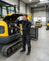 Ein Mechaniker in schwarzer Arbeitskleidung repariert einen gelben Minibagger in einer Werkstatt.