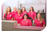 Artzhelferinnen in pinkfarbenen Poloshirts stehen hinter oder vor einem Empfangstresen.