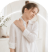 A woman in a white blouse closes her eyes and massages her shoulder to relieve pain.