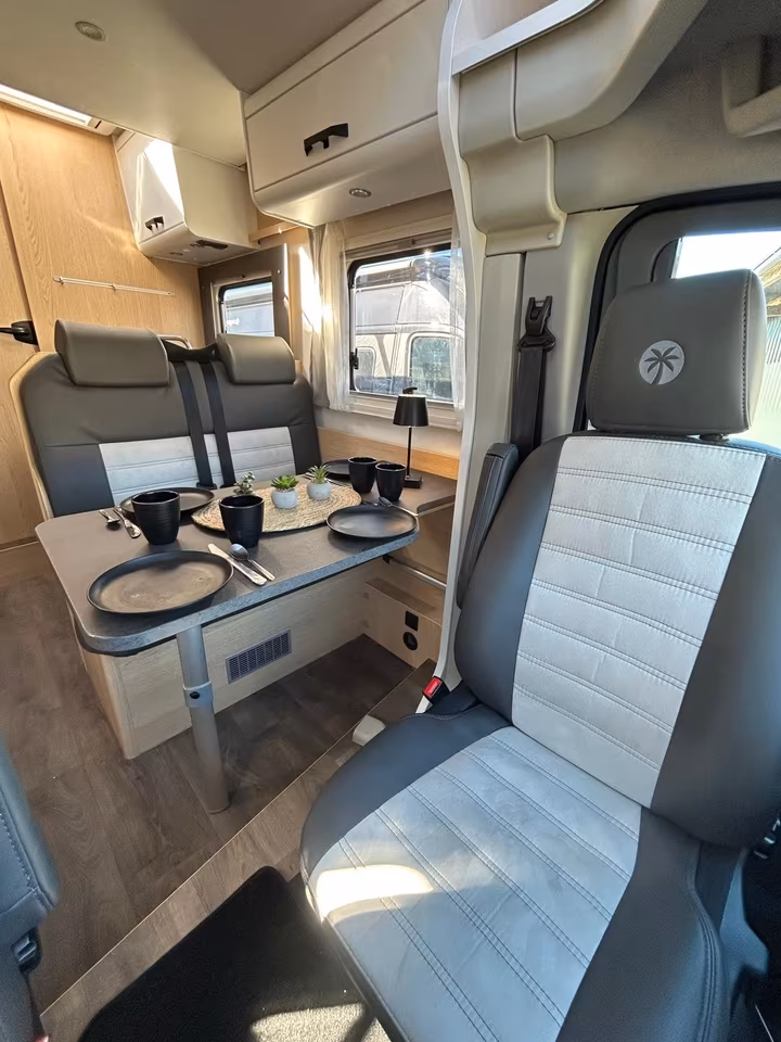 Innenansicht eines Wohnmobils mit Esstisch, zwei Sitzbänken und drehbarem Fahrersitz.