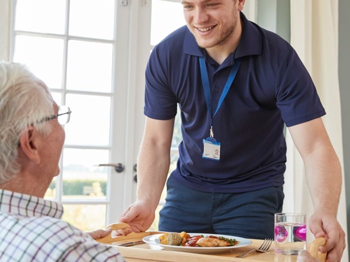 Mitarbeiter bringt einem Senior das Mittagessen