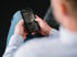 Nahaufnahme eines Mannes in hellem Hemd und Jeans, der ein schwarzes Smartphone mit einer App in den Händen hält.