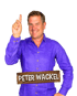 Peter Wackel im lila Hemd zeigt mit dem Zeigefinger nach oben; Namenszug auf Holzschild im Vordergrund.