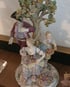 Farbige Porzellanfigur mit Baum, Mann im Dreispitz, Frau mit Blumenkorb und Kind.