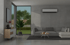 Modernes Wohnzimmer mit Klimaanlage über einem grauen Sofa, Couchtisch und Blick auf einen Garten.