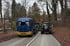 Blauer Mercedes-Lkw und ein Traktor stehen für Waldarbeiten auf einer schmalen Straße am Waldrand.