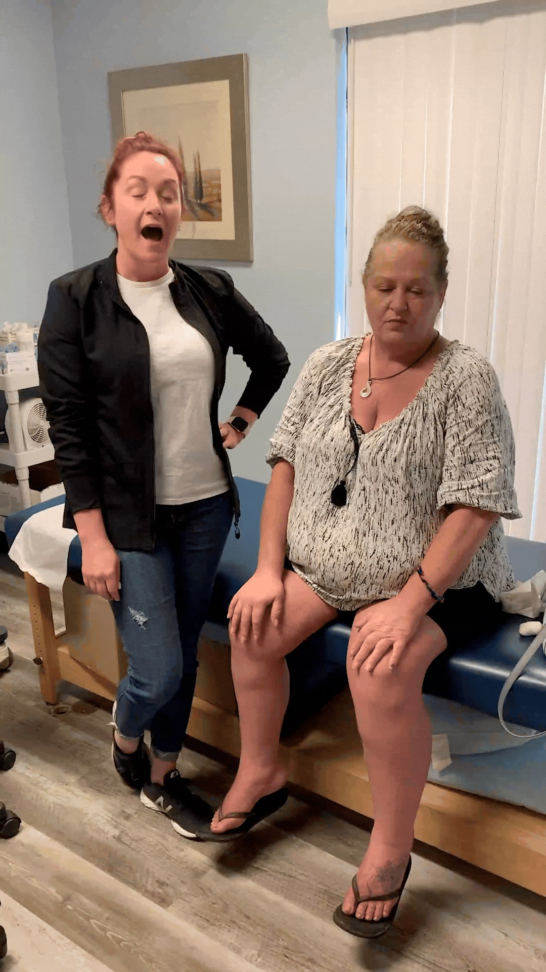 Patient seated on a treatment table with hands on her knees beside a PC Medical Centers staff member in an exam room