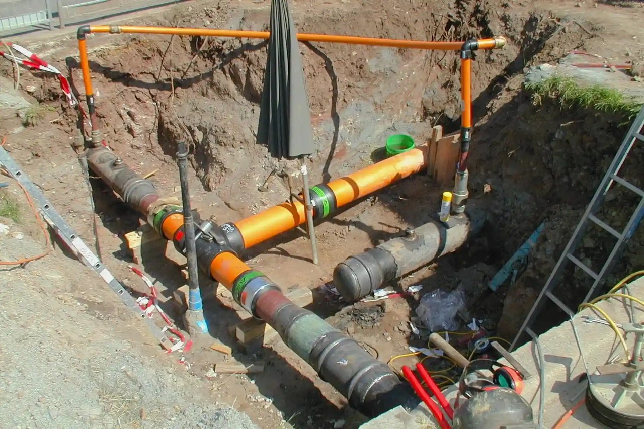 Baustelle mit freigelegten orangefarbenen und grauen Gasrohren in einer Grube.
