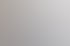 Ein lächelnder Mann in Anzug und Brille lehnt sich an eine weiße Wand.