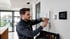 Techniker installiert eine Alarmanlage an einer Wand neben einem Smart-Home-Display und einem Bewegungsmelder.