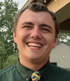 Young man with brown hair and a green shirt with a yellow, green, and black striped tie, smiling.
