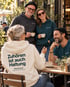 Vier Menschen an einem Cafétisch, im Vordergrund ein cremefarbener Wearmorrow® Hoodie mit der Rückenbotschaft Zuhören ist auch Haltung