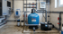 Schwimmbad-Filteranlage mit blauem Filtertank, Pumpen, Rohren und Steuerungselementen in einem Technikraum.