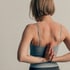 Frau mit kurzen Haaren, Yoga-Top und Händen in Gebetshaltung hinter dem Rücken.