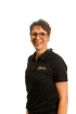 Frau mit Brille, kurzem Haar und schwarzem Poloshirt mit dem Logo "Muehlbauer" lächelt.