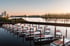 Moderne weiße Hausboote liegen in Reih und Glied an einem Steg im Hafenbecken bei Sonnenuntergang.