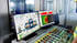 Two monitors displaying industrial control software next to a panel with colorful buttons and a hand.
