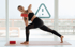 Frau in schwarzer Sportkleidung macht Yoga-Übungen mit roten Blöcken auf einer Matte vor einer Fensterfront.
