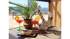 Zwei Aperol Spritz und Snacks auf einem Tisch mit einem Anker und einer Palme vor einem Strand in der Villa Aperol.