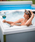 Frau mit Sonnenbrille und Strohhut entspannt sich in einem Whirlpool und hält ein blaues Getränk.