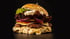 Doppelter Cheeseburger mit Salat, Tomaten, Zwiebeln und Feta-Käse auf schwarzem Hintergrund.