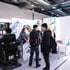Besucher an einem Messestand von Junobau mit CAT-Simulator und Werbewänden in einer Industriehalle.