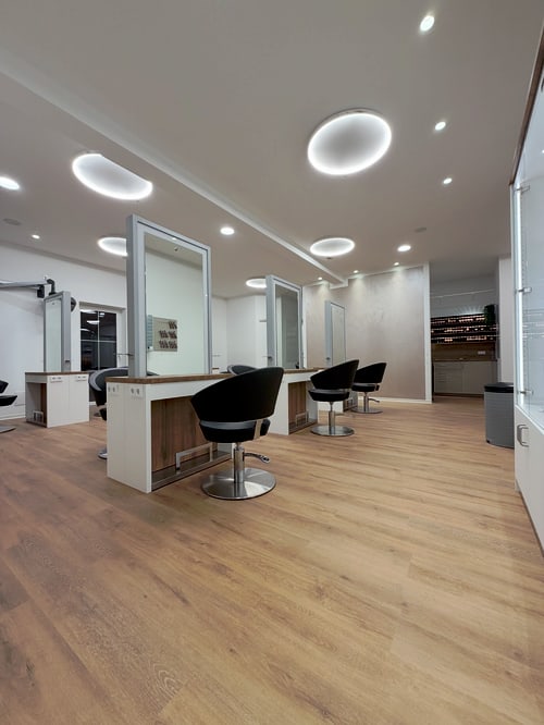 Friseursalon mit Holzboden, drei Arbeitsplätzen mit Spiegeln und schwarzen Stühlen.