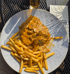 Ein Teller mit Schnitzel in Rahmsoße mit Pilzen und Pommes Frites auf einem dunklen Metalltisch.