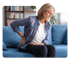 Woman clutching lower back and hip while sitting on a blue couch`