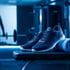 Dunkelblaue Turnschuhe und ein gerolltes Handtuch liegen auf einer Hantelbank in einem blau beleuchteten Fitnessstudio.