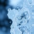 Wasserspritzer und Tropfen schweben vor einem unscharfen blauen Hintergrund.