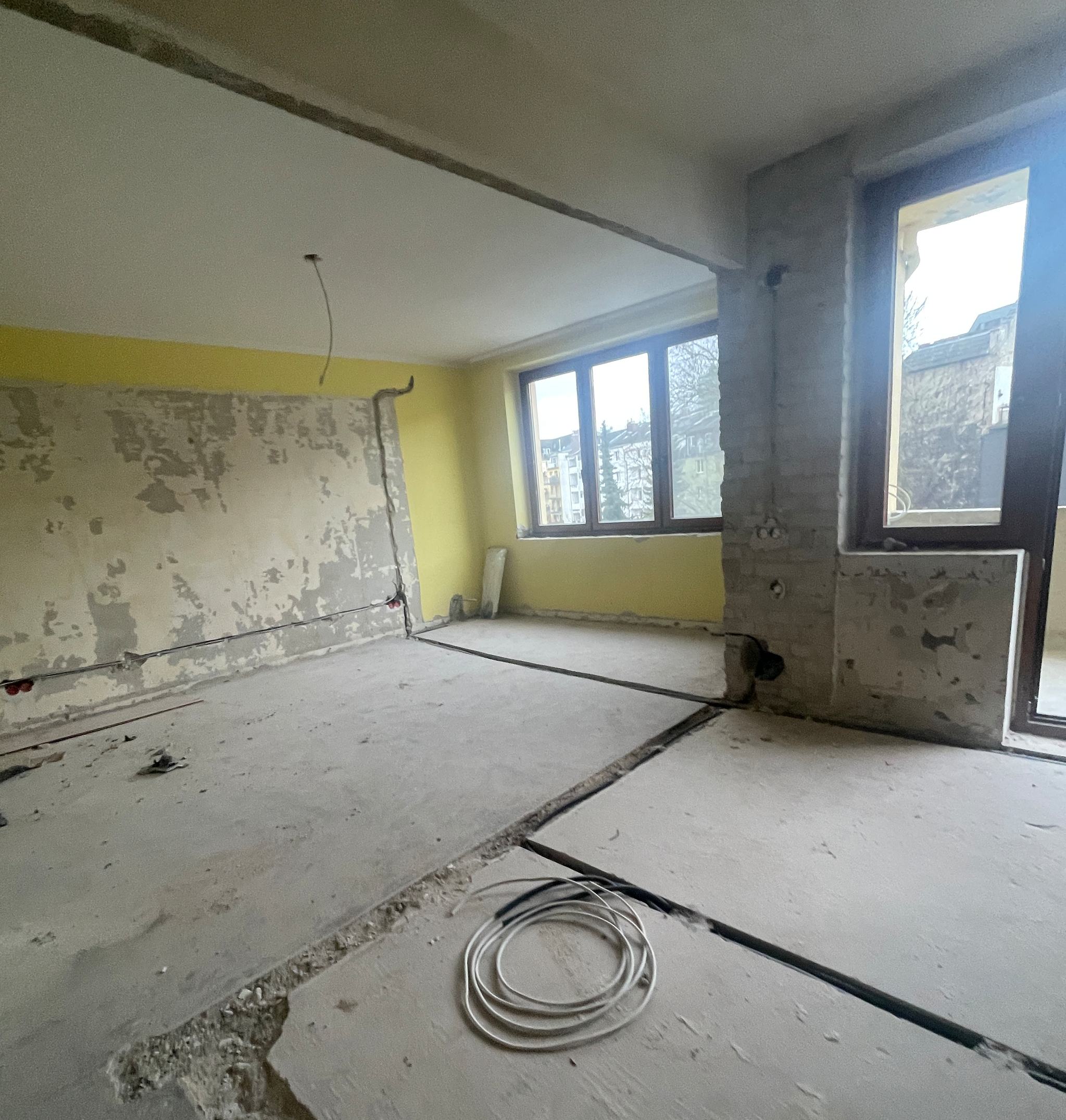 Wohnzimmer im Rohbau mit freiliegenden Kabeln, offenen Wänden und unebenen Estrichboden vor der Renovierung