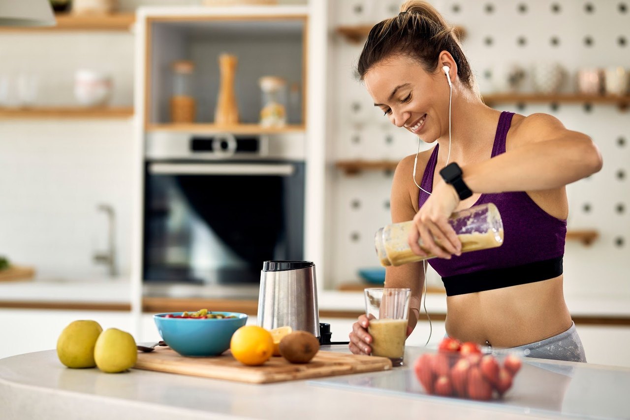 Junge Frau bereitet sich in ihrer Küche einen Fruchtsmoothie zu