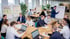 Ein Team von 14 Personen arbeitet in einem hellen Büro an Tischen und Flipcharts zusammen.