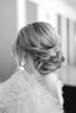 Rückansicht einer eleganten Hochsteckfrisur einer Braut mit Perlen-Haarschmuck und flauschigem Bolero in Schwarz-Weiß.