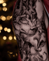 Detailliertes schwarz-graues Wolf-Tattoo im ornamentalen Stil auf einem Oberarm mit Perlenketten und floralen Elementen.