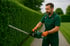 Gärtner in Arbeitskleidung und Handschuhen schneidet eine Hecke mit einer Heckenschere.