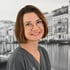 Lächelnde junge Frau mit Brille und grauer Uniform vor einer Schwarz-Weiß-Aufnahme von Venedig.