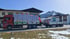 Ein roter LKW mit Anhänger, beladen mit weißen Paketen, steht vor einem Gebäude mit einem schneebedeckten Berg im Hintergrund.
