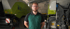 Ein lächelnder Mann mit Brille in grüner Arbeitskleidung steht vor landwirtschaftlichen Maschinen in einer Halle.